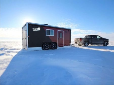 Black truck is pulling a Yetti Fish House Traxx Edition across a snow covered frozen lake